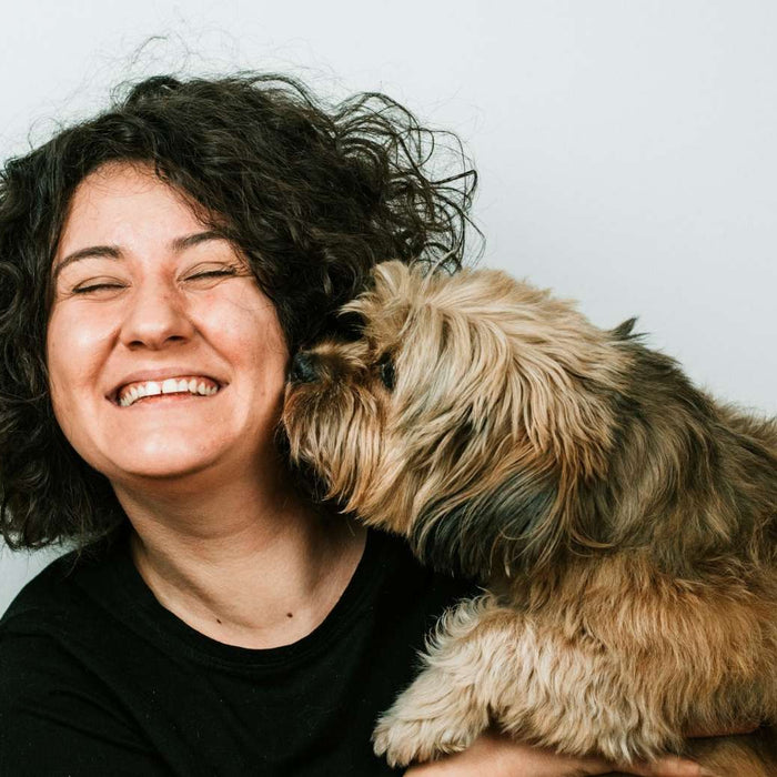 A curly-haired woman holds her dog close while it sniffs her face, hinting at the bond explored in Can Dogs Sense Health Problems in Humans