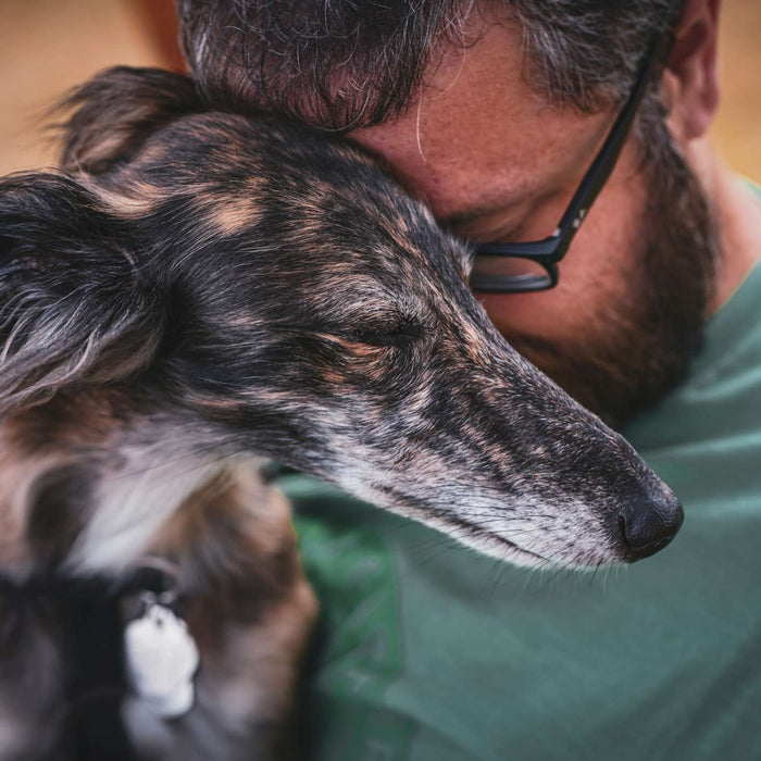 A man presses his forehead to his dog’s head as they rest together with closed eyes, capturing the quiet pain and love in how to heal after saying goodbye to your dog