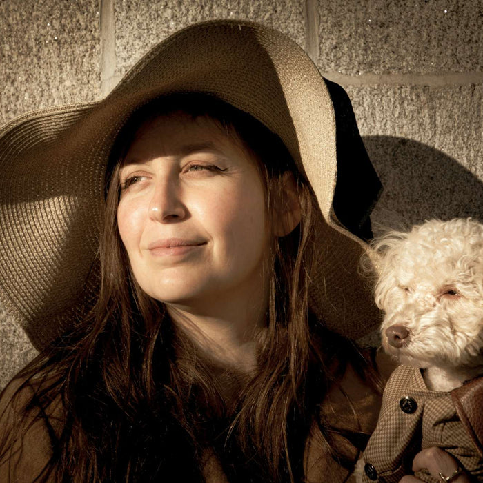 Calm woman cuddles her tiny coated dog by a stone wall, showing the bond behind are dogs good for human health