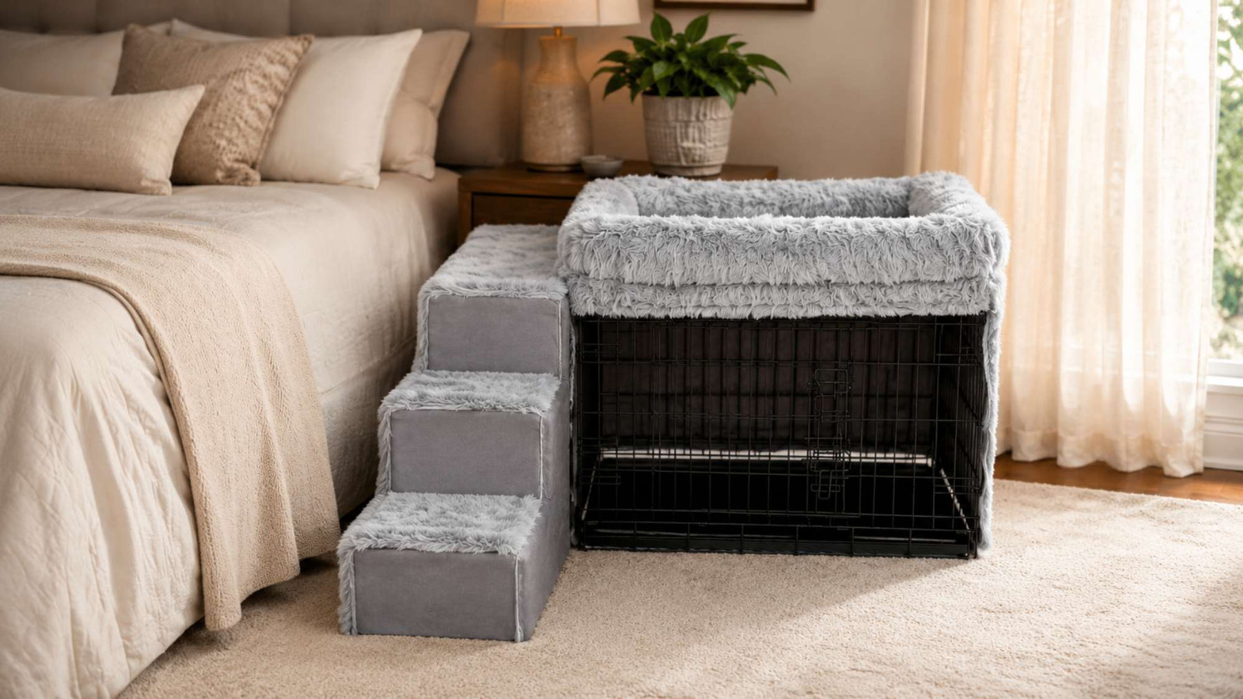 Gray bedside dog bed with plush stairs and a raised cushioned sleeper sits parallel beside a neatly made bed over a black wire crate