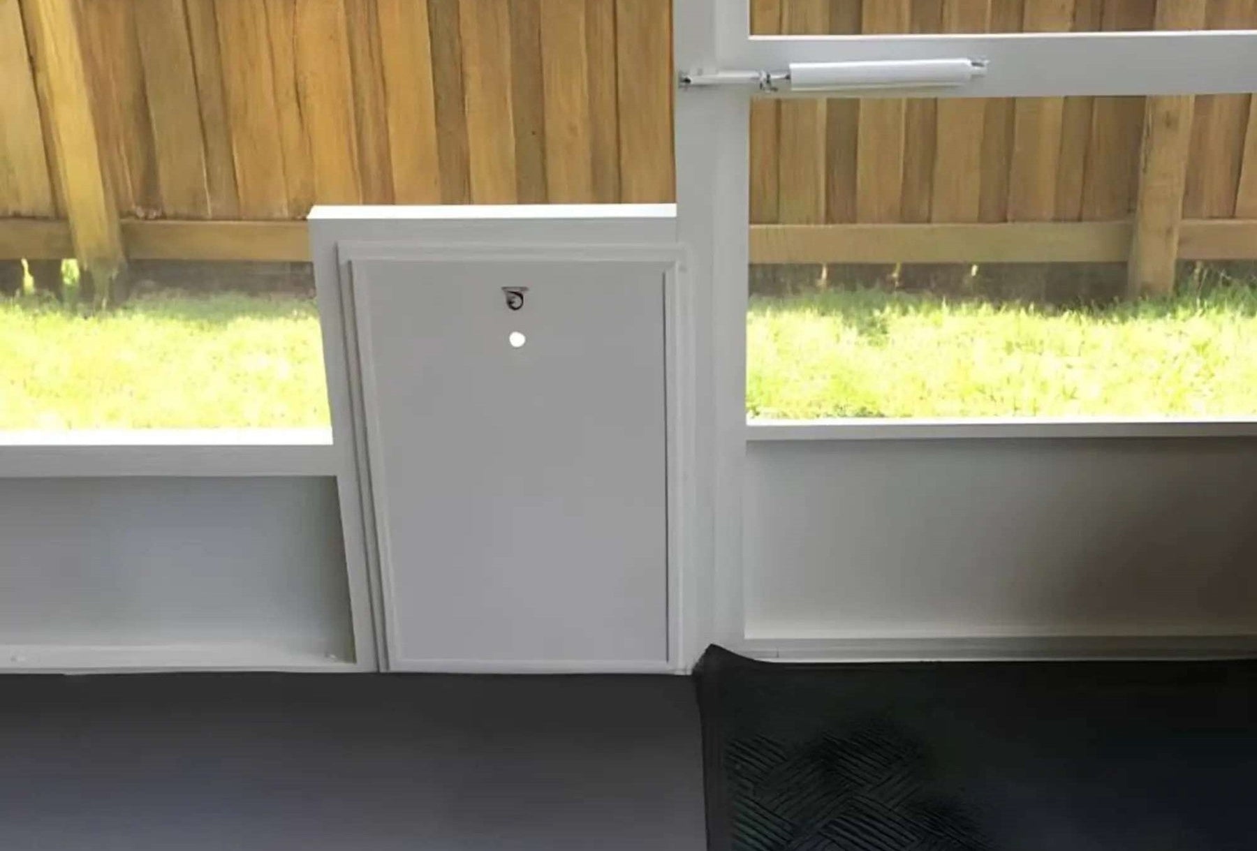 White puppy dog door with a locking panel installed in a screened enclosure providing secure access to a fenced backyard