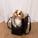 A Cavalier King Charles Spaniel sitting inside the Paw PupTote™ 3-in-1 Faux Leather Dog Carrier Bag - Black with a white curtain backdrop