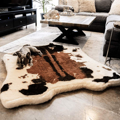 A French bulldog naps on the Brown Faux Cowhide Paw PupRug™ Animal Print Memory Foam Dog Bed in a stylish living room