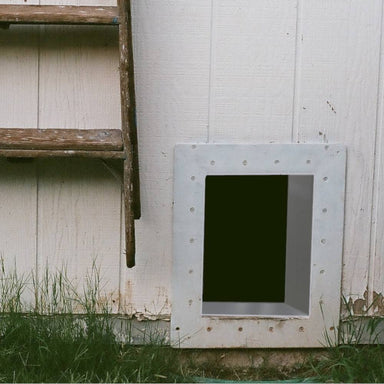 A Security Boss Trim-To-Fit Wall Tunnel Insert installed in an exterior wall, showing the metal tunnel framed by screws, providing a secure and weather-proof passage through the wall