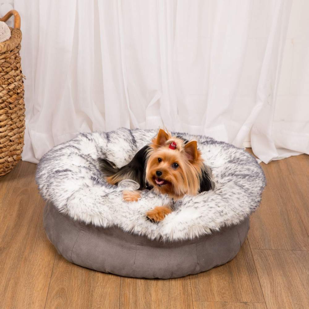 A Yorkshire Terrier is relaxing on the Ultra Plush Arctic Fox Paw PupPouf™ Luxe Faux Fur Donut Dog Bed on a wooden floor