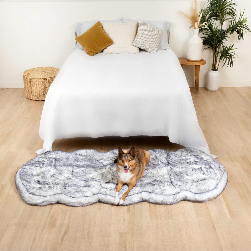 A brown and white dog lying on a Paw PupRug™ Runner Faux Fur Memory Foam Dog Bed Ultra Plush Arctic Fox at the foot of a white bed in a minimalist bedroom