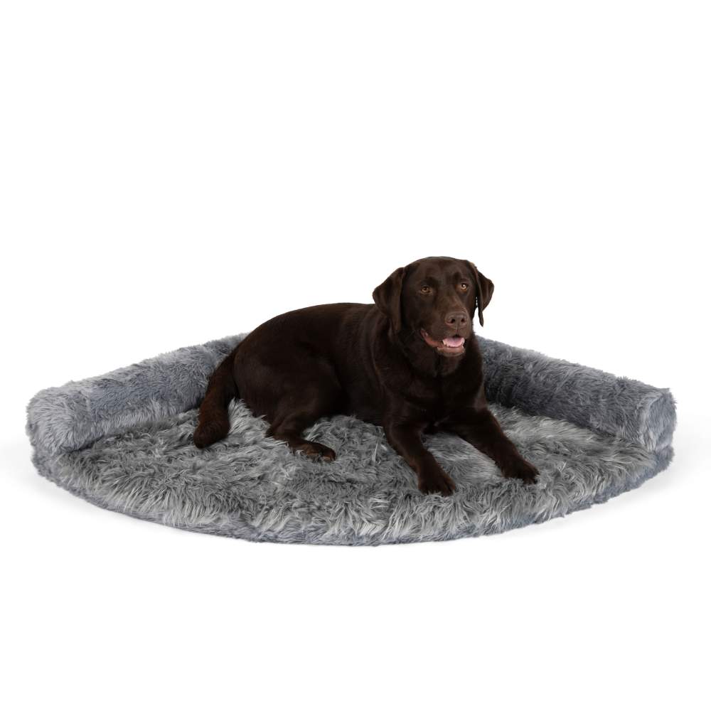 A chocolate Labrador is sitting on the Charcoal Grey Paw PupRug™ Memory Foam Corner Dog Bed against a white background