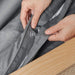 A close-up of hands holding a buttoned area of the bedding, highlighting the details of the Paw PupSheets™ Hair Resistant, Antimicrobial, & Cooling Duvet Cover and Sheet Set Bundle - Graphite