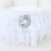 A close-up of the decorative brooch on the Hello Doggie Crib Dog Bed in white, featuring intricate lace ruffles and gleaming crystal embellishments