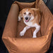 A content dog is lying in the Paw PupProtector™ Faux Leather Memory Foam Dog Car Bed - Camel Pet Bed, placed in a car seat for safe travel