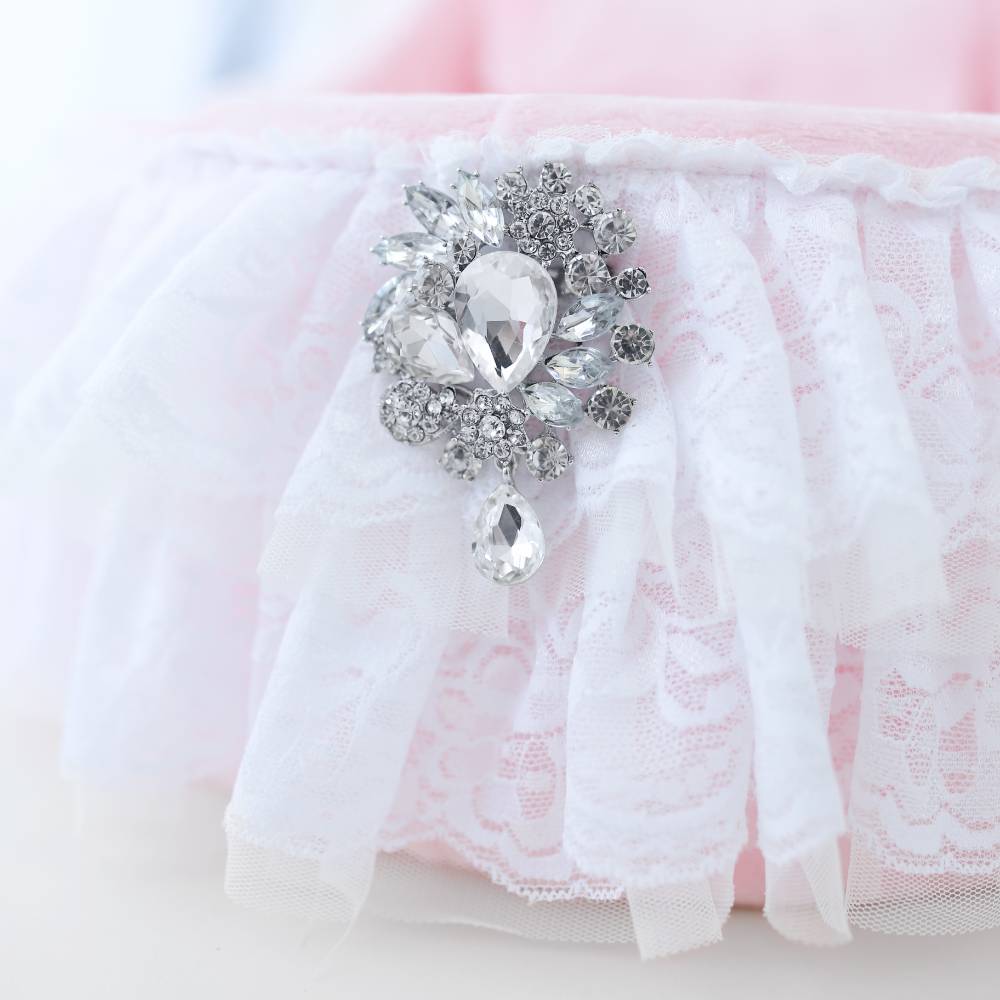 A detailed view of the elegant brooch on the Hello Doggie Crib Dog Bed in pink, highlighting the delicate lace ruffles and shiny crystal decorations