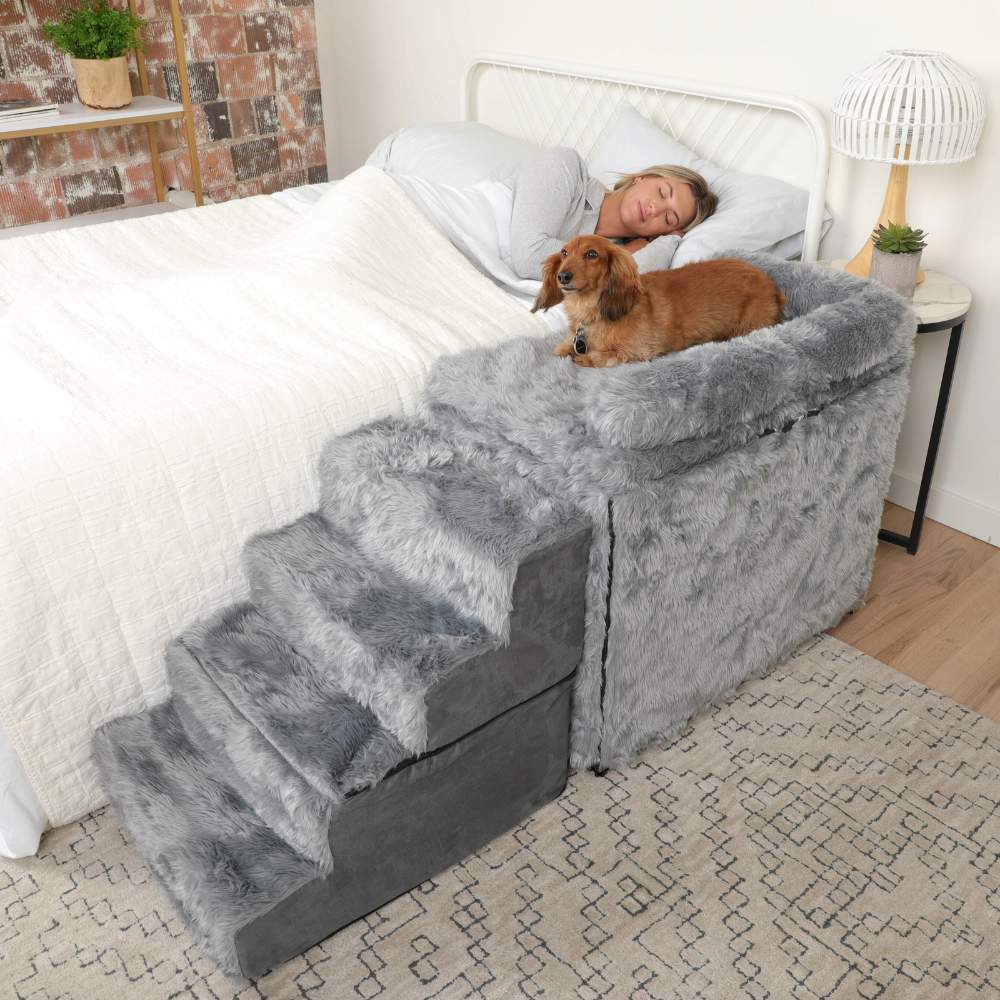 A dog is lying on the Paw Pet Bedside Sleeper Crate Kit & Stairs while a woman sleeps in the bed next to it