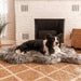 A dog is resting on the Curve Charcoal Grey Paw PupRug Faux Fur Orthopedic Dog Bed in front of a white brick fireplace