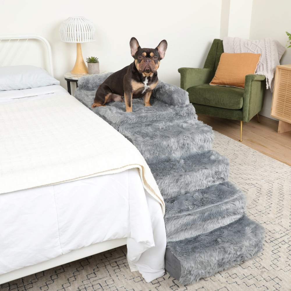 A dog is sitting at the top of the Paw Pet Bedside Sleeper Crate Kit & Dog Stairs next to a bed