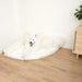 A fluffy white dog is lying on the Polar White Paw PupRug™ Memory Foam Corner Dog Bed in a room corner