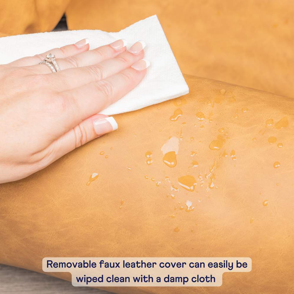 A hand is wiping the removable faux leather cover of the Paw PupProtector™ Faux Leather Memory Foam Dog Car Bed - Camel, which can be easily cleaned with a damp cloth