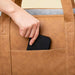 A hand placing a phone into the exterior pocket of the Paw PupTote™ 3-in-1 Faux Leather Dog Carrier Bag - Camel