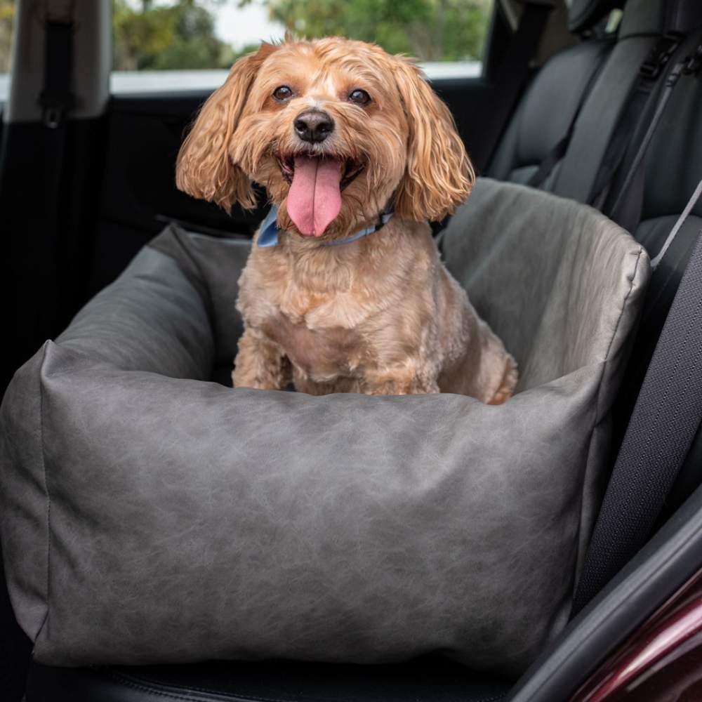 A happy dog is sitting in the Paw PupProtector™ Faux Leather Memory Foam Dog Car Bed - Slate Gray Double Seat Pet Bed, placed in a car seat