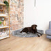 A large chocolate Labrador is relaxing on the Charcoal Grey Paw PupRug™ Memory Foam Corner Dog Bed, placed against a wall with a rustic brick design