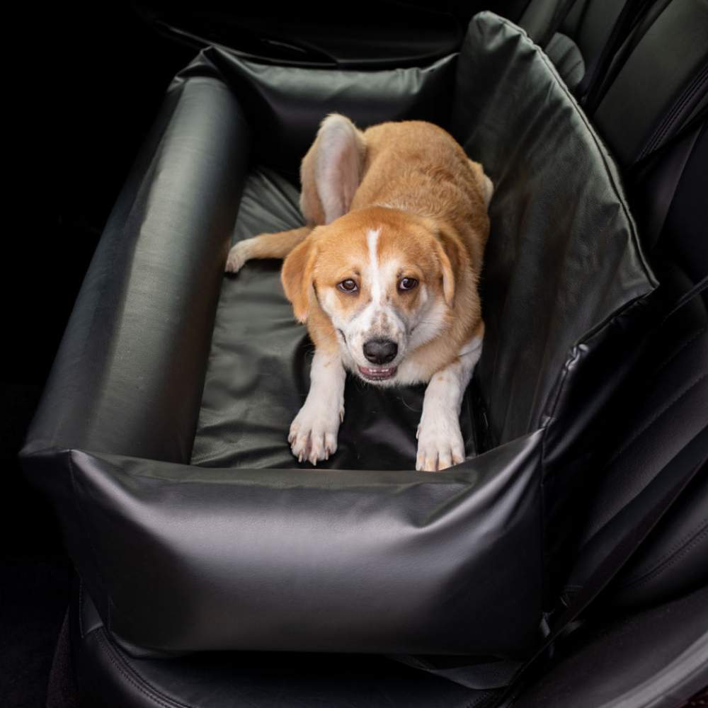 A medium-sized dog is lying down on the back seat, secured and relaxed in the Paw PupProtector™ Faux Leather Memory Foam Dog Car Bed - Black