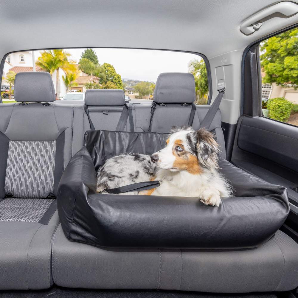 A medium-sized dog is sitting securely on the back seat, enjoying the Paw PupProtector™ Faux Leather Memory Foam Dog Car Bed - Black Double Seat Doggie Bed