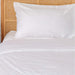 A neatly made bed with a rattan headboard and white bedding highlighting the Paw PupSheets™ Hair Resistant, Antimicrobial, & Cooling Bed Sheet Set - White