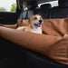 Another dog is pictured enjoying the comfort of the Paw PupProtector™ Faux Leather Memory Foam Dog Car Bed - Camel Full Back Seat, situated in the back seat of a car