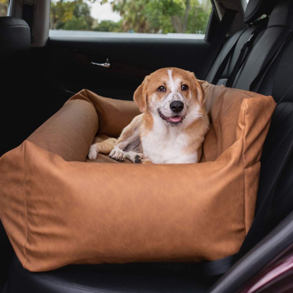 Another dog is relaxing in the Paw PupProtector™ Faux Leather Memory Foam Dog Car Bed - Camel Dull Back Vehicle Seat, placed in a car seat