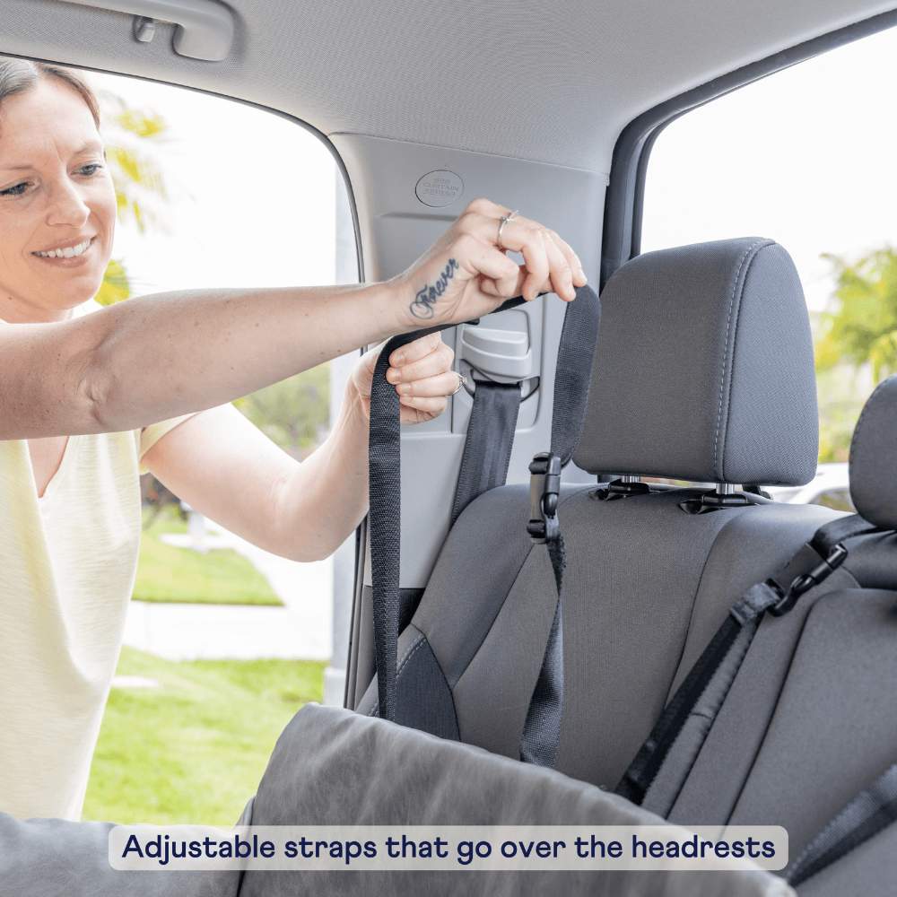 A person is adjusting the headrest straps for a Paw PupProtector™ Memory Foam Dog Car Bed in a car