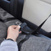 A person is fastening the seatbelt to secure the Paw PupProtector™ Memory Foam Dog Car Bed in the car