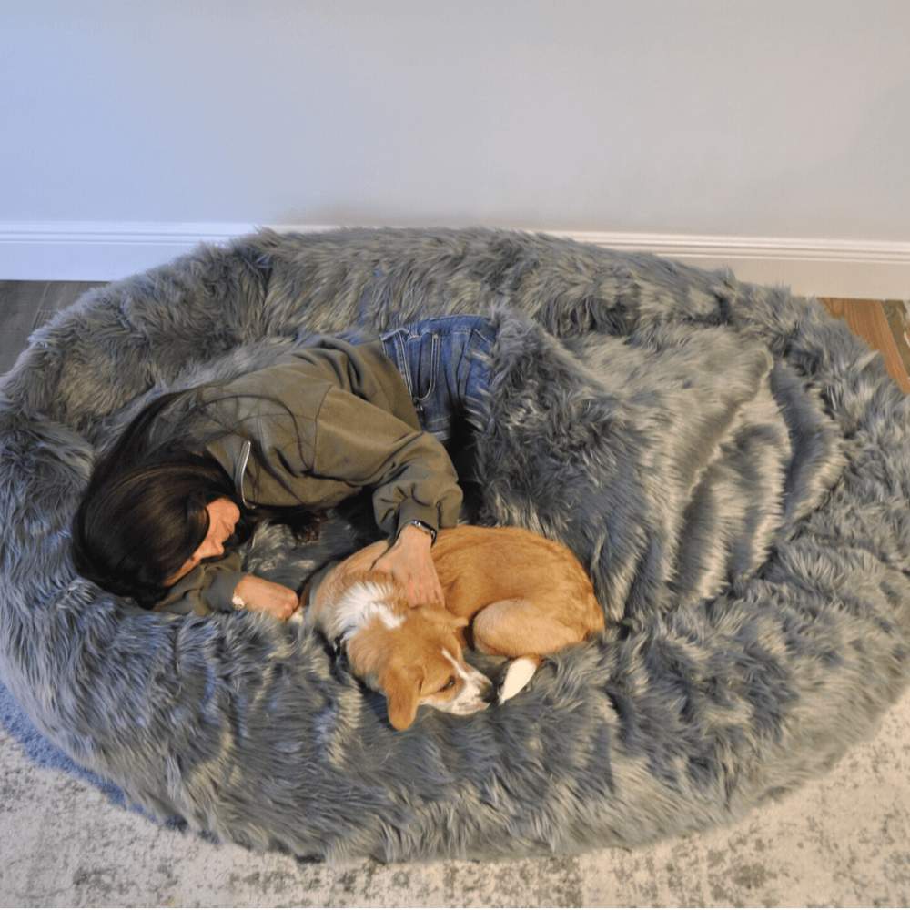 A person naps peacefully with a small dog on the Charcoal Grey Paw PupCloud™ Human-Size Faux Fur Memory Foam Dog Bed