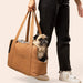A pug being carried by a person in the Paw PupTote™ 3-in-1 Faux Leather Dog Carrier Bag - Camel, with only the person's legs visible