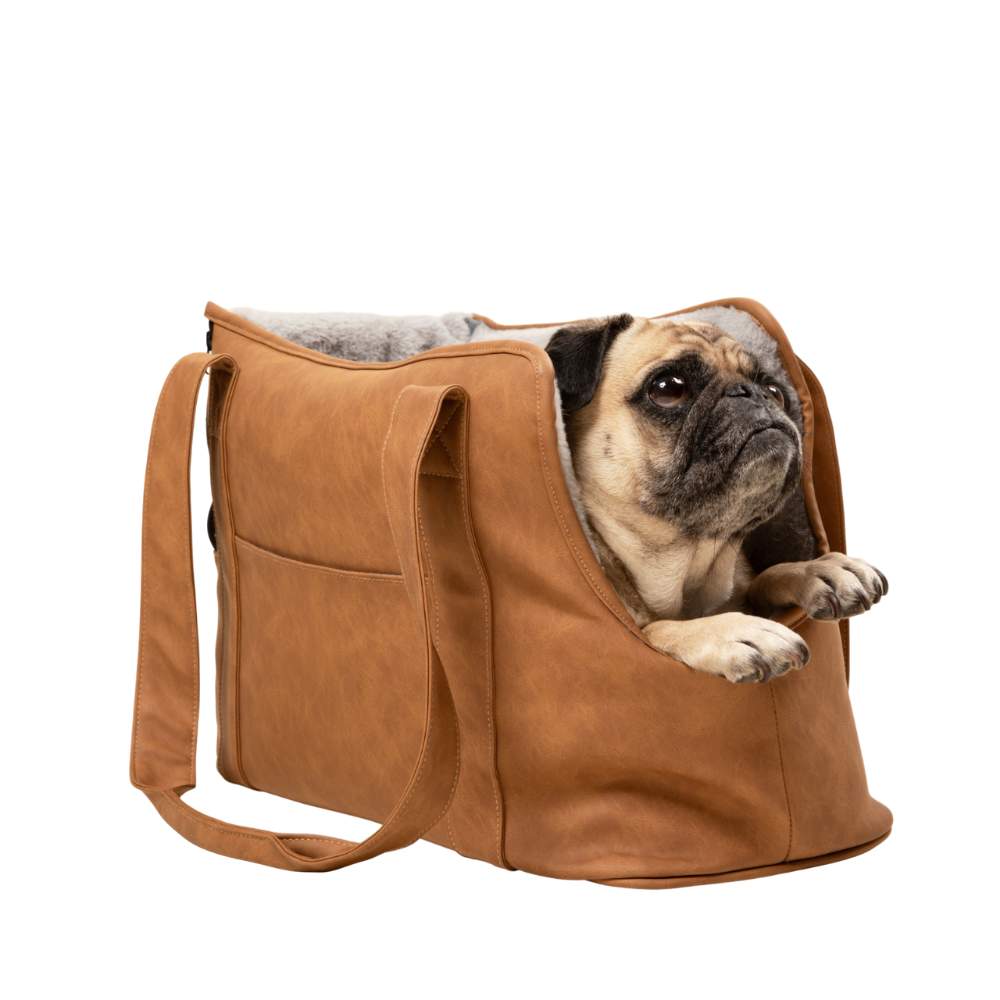 A pug looking up while sitting in the Paw PupTote™ 3-in-1 Faux Leather Dog Carrier Bag - Camel against a plain white background