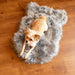 A small brown dog is lying comfortably on the Curve Charcoal Grey Paw PupRug Faux Fur Orthopedic Dog Bed, placed on a wooden floor