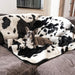 A small dog is lying on a grey sofa covered with the Paw PupProtector™ Waterproof Throw Blanket - Black Faux Cowhide Dog Blanket For Couch
