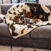 A small dog is lying on a grey sofa covered with the Paw PupProtector™ Waterproof Throw Blanket - Brown Faux Cowhide Dog Blanket For Couch