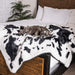 A small dog is resting on a bed with the Paw PupProtector™ Waterproof Throw Blanket - Black Faux Cowhide Best Dog Blanket