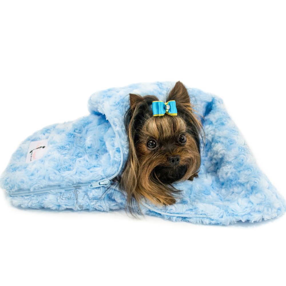 A small dog laying on a blue Hello Doggie Snuggle Pup Sleeping Bag, with the bag partially unzipped