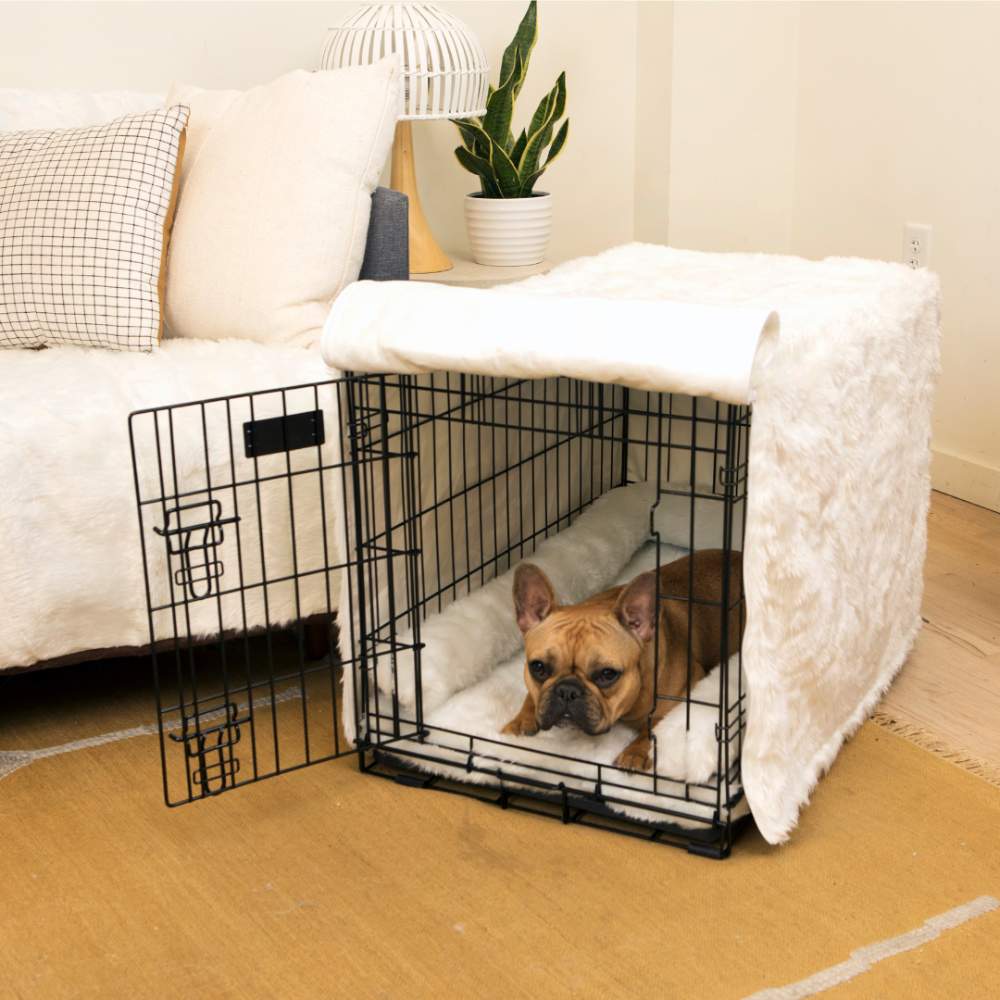 A small dog lies inside a black wire crate covered with white fabric, showcasing the cozy setup from the Paw Upgrade Your Dog Crate Kit - Polar White
