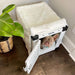 A small dog peeks out from inside a white crate covered with a fluffy white blanket, part of the Paw Upgrade Your Dog Crate Kit - Polar White