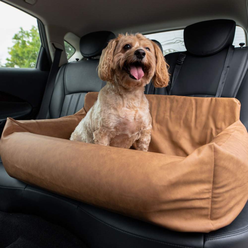 A small dog sits happily in the back seat, secured in the Paw PupProtector™ Faux Leather Memory Foam Dog Car Bed - Camel Double Car Seat