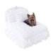 A small dog sitting comfortably on the Hello Doggie Enchanted Nights Dog Bed in white, which features fluffy cushions, ruffled edges, and white satin bows with crystal centers