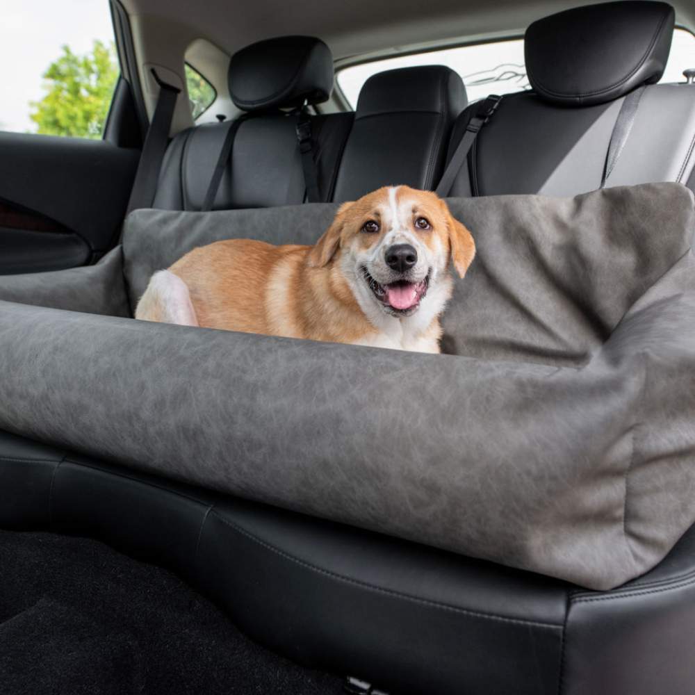 A smiling dog is lounging in the back seat, secured in the Paw PupProtector™ Faux Leather Memory Foam Dog Car Bed - Slate Gray Doggie Bed