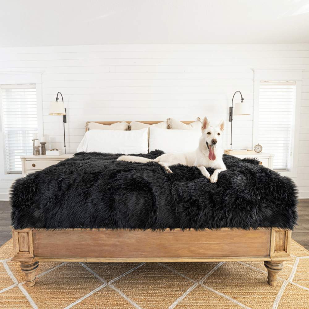 A white dog is comfortably lying on a bed covered with a Paw PupProtector™ Waterproof Throw Blanket - Midnight Black