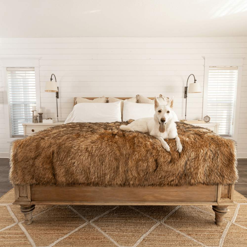 A white dog is lounging on a bed covered with a Paw PupProtector™ Waterproof Throw Blanket - Sable Tan