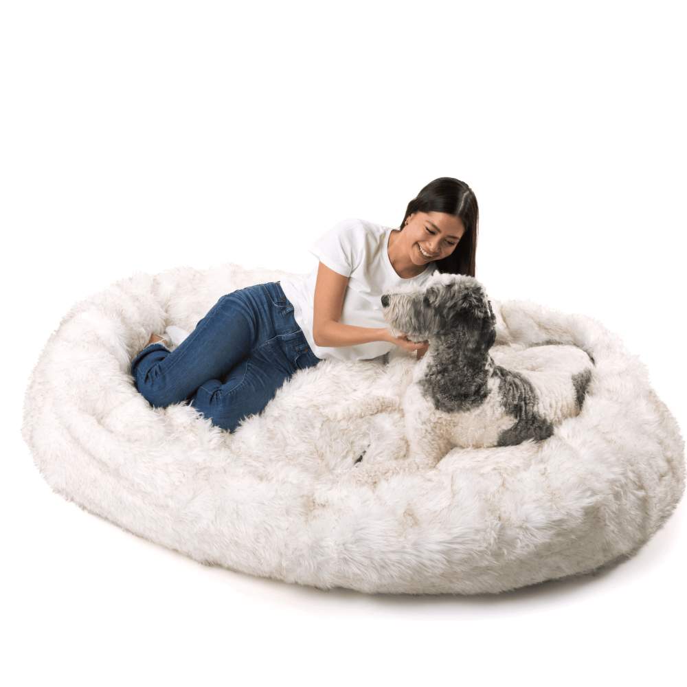 A woman affectionately pets her dog while lounging on the White with Brown Accents Paw PupCloud™ Human-Size Faux Fur Memory Foam Dog Bed