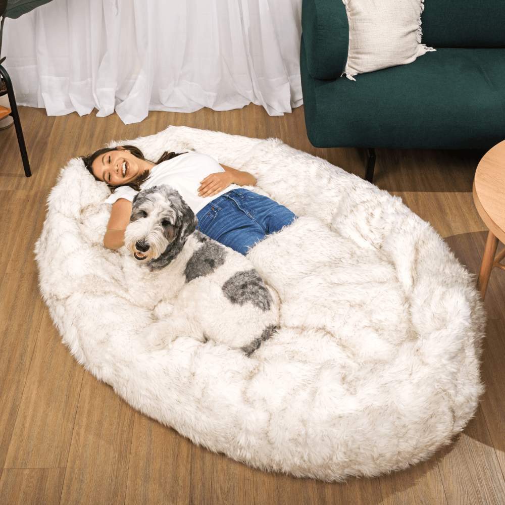 A woman and a dog rest contentedly on a White with Brown Accents Paw PupCloud™ Human-Size Faux Fur Memory Foam Dog Bed