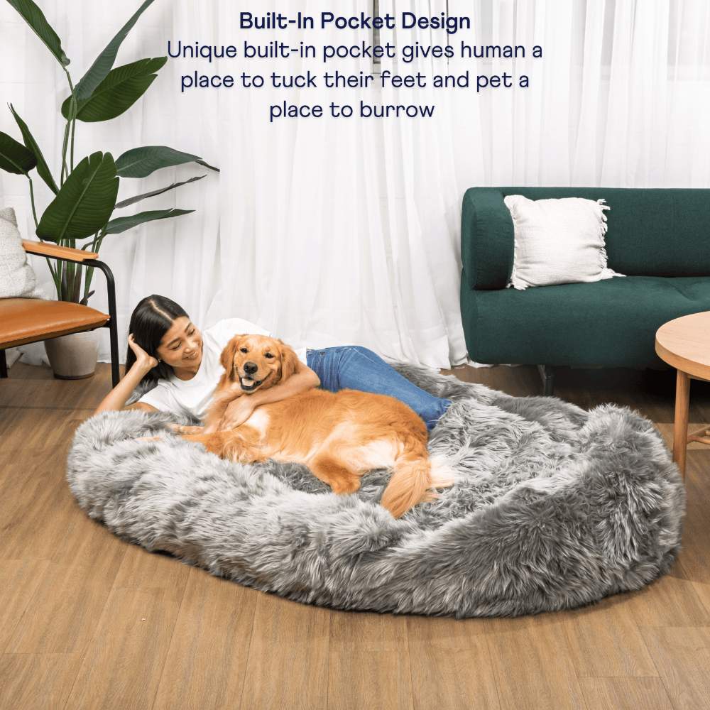 A woman and her golden retriever relax on a Charcoal Grey Paw PupCloud™ Human-Size Faux Fur Memory Foam Dog Bed with a built-in pocket design for added comfort
