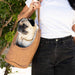 A woman carrying a pug in the Paw PupTote™ 3-in-1 Faux Leather Dog Carrier Bag - Camel with a leafy background