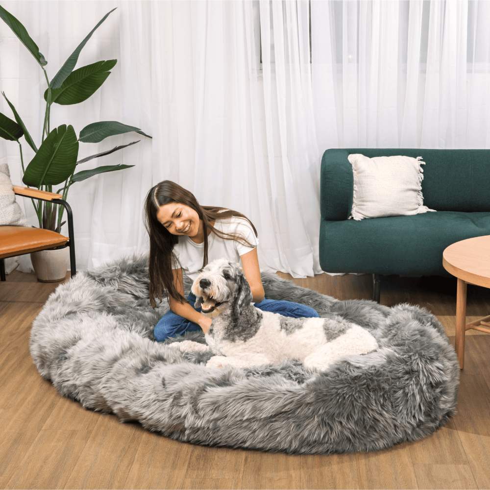 A woman enjoys a tender moment with her dog on a Charcoal Grey Paw PupCloud™ Human-Size Faux Fur Memory Foam Dog Bed